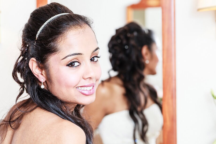 a smiling bride turns from the mirror to pose for a photograph
