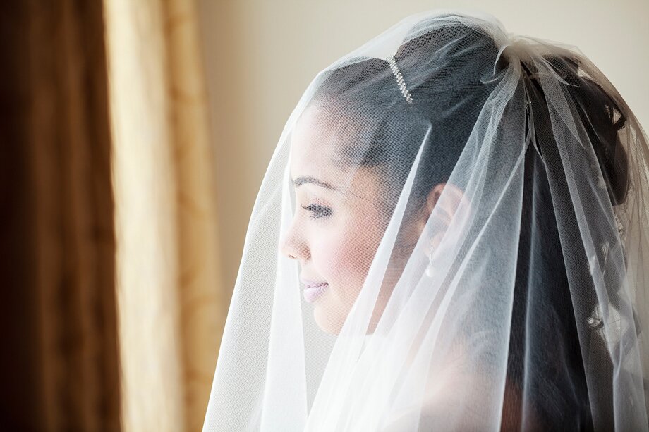 a bride wearing a veil looks out of a window